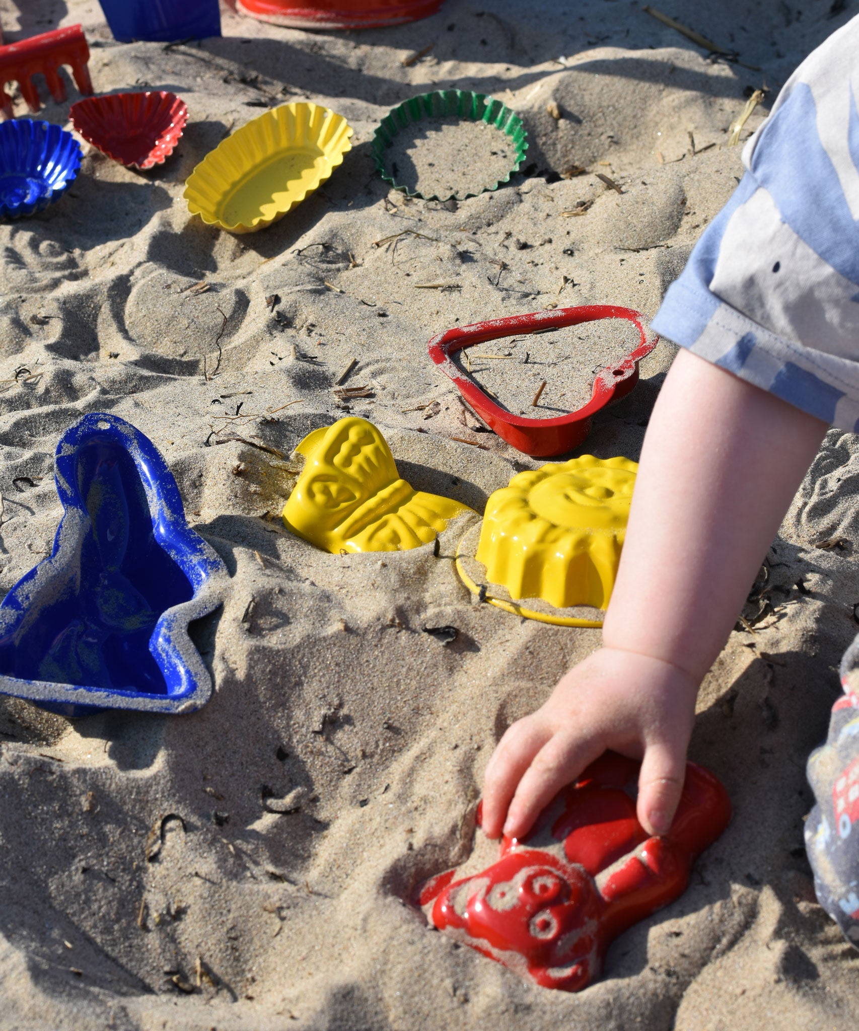 A child placing a red teddy shaped mould in the sand surrounded by  other shaped moulds in the background.