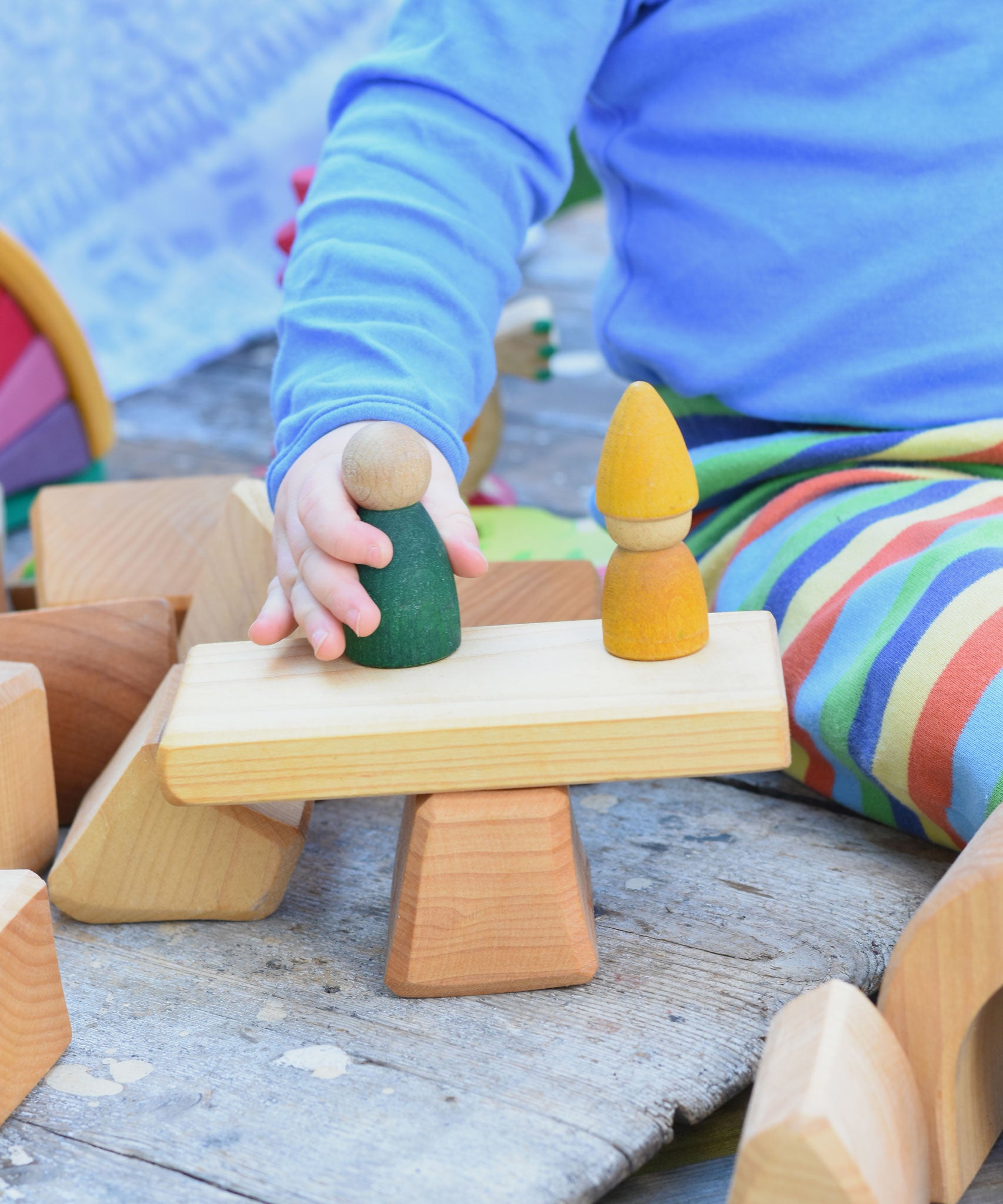 Two blocks from the Glückskäfer 17 Large Natural Blocks set used to create a pretend seesaw for wooden peg dolls. 