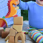 A child placing a Holztiger dragon on a pile of blocks from the Glückskäfer 17 Large Natural Blocks Set.