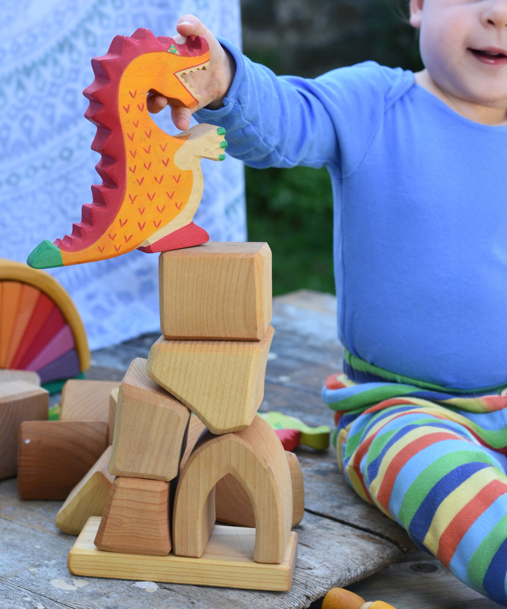 A child placing a Holztiger dragon on a pile of blocks from the Glückskäfer 17 Large Natural Blocks Set.