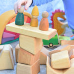 A child placing Wooden peg dolls on a stack of blocks from the Glückskäfer 17 Large Natural Blocks set. 