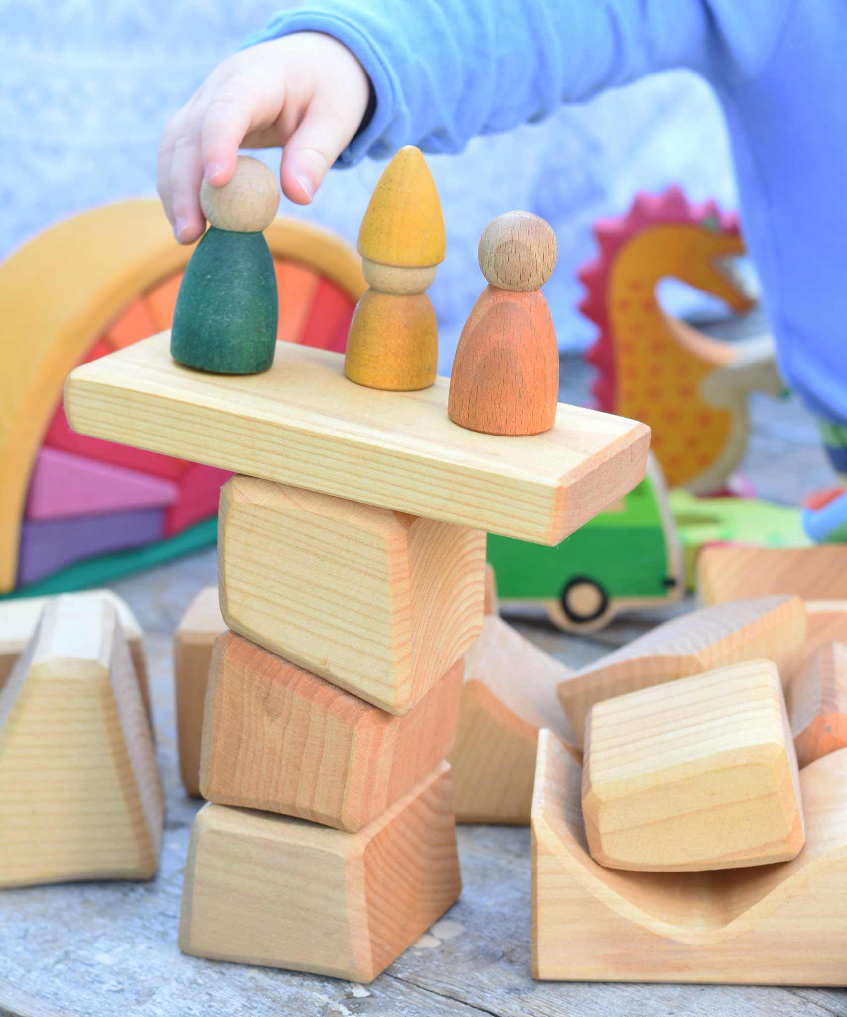 A child placing Wooden peg dolls on a stack of blocks from the Glückskäfer 17 Large Natural Blocks set. 
