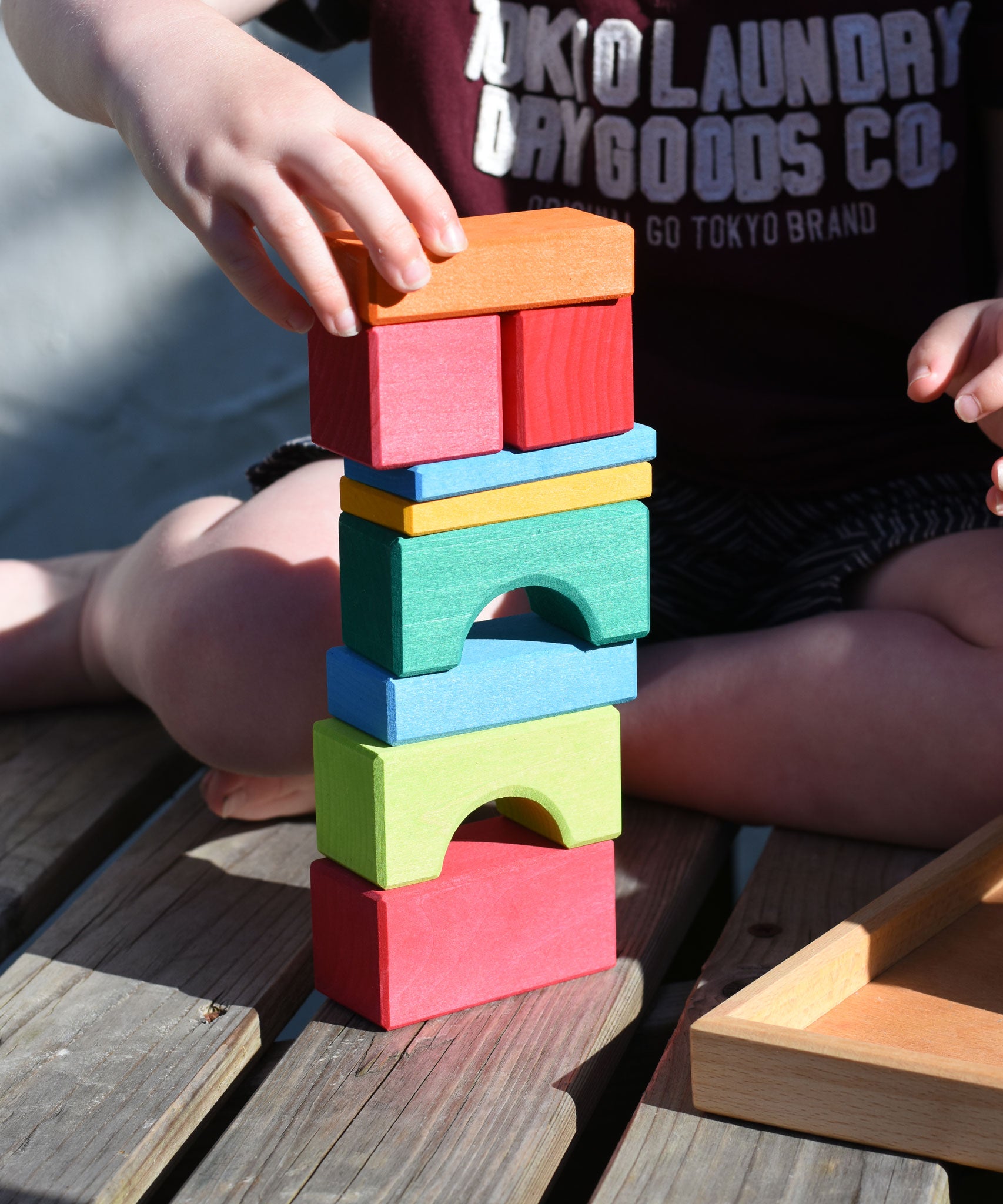 A close up of a child stacking wooden toy blocks on top of each other. The blocks are from the Glückskäfer 20-Piece Small Toscana Blocks Set. 