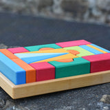 The Glückskäfer 20-Piece Small Toscana Blocks Set shown with the wooden blocks perfectly placed in their wooden storage tray on a stone wall outdoors. 