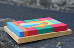 The Glückskäfer 20-Piece Small Toscana Blocks Set shown with the wooden blocks perfectly placed in their wooden storage tray on a stone wall outdoors. 