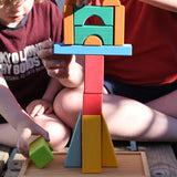 Two children creating a tower by stacking wooden to building block from the Glückskäfer 20-Piece Small Toscana Blocks Set on top of each other. 