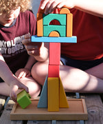 Two children creating a tower by stacking wooden to building block from the Glückskäfer 20-Piece Small Toscana Blocks Set on top of each other. 