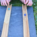 A close up of a child's hand's racing two marbles down two pieces of track from the Glückskäfer 23 Piece Wooden Marble Track set.
