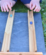 A close up of a child's hand's racing two marbles down two pieces of track from the Glückskäfer 23 Piece Wooden Marble Track set.