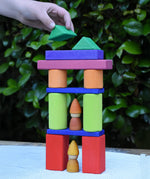 A child playing with the Glückskäfer 53 piece big provence wooden blocks set creating a tower with Grapat tomten nins placed inside.