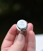 Close up of the 100g weight from the Glückskäfer balance with weights children's weighing scales toy in an adults hand. 