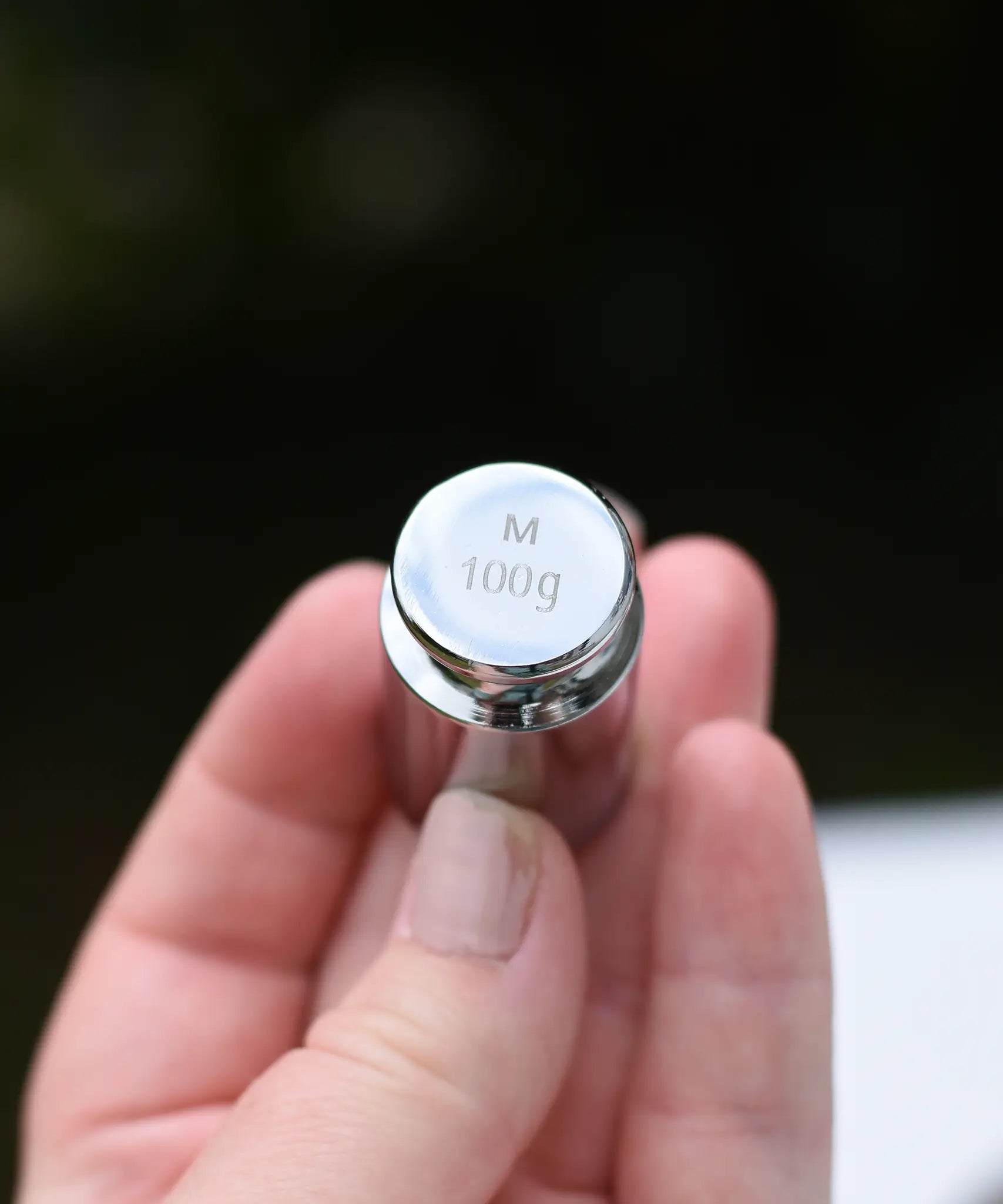 Close up of the 100g weight from the Glückskäfer balance with weights children's weighing scales toy in an adults hand. 