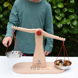 Cjild placing weights onto one side of teh Glückskäfer balance with weights children's weighing scales toy with Grapat mandala mushrooms on the other side.