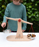 Cjild placing weights onto one side of teh Glückskäfer balance with weights children's weighing scales toy with Grapat mandala mushrooms on the other side.