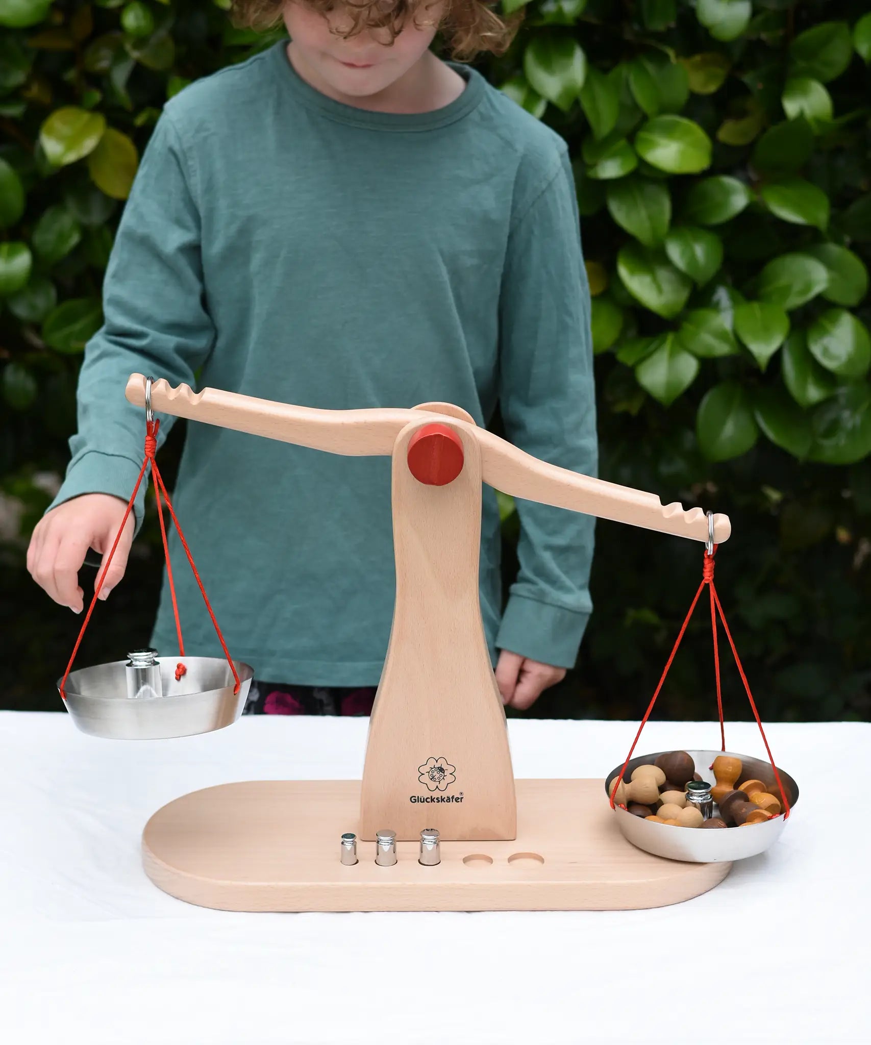 Cjild placing weights onto one side of teh Glückskäfer balance with weights children's weighing scales toy with Grapat mandala mushrooms on the other side.