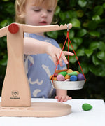 Child placing Grapat mandlaa pieces onto the Glückskäfer balance with weights children's weighing scales toy.  