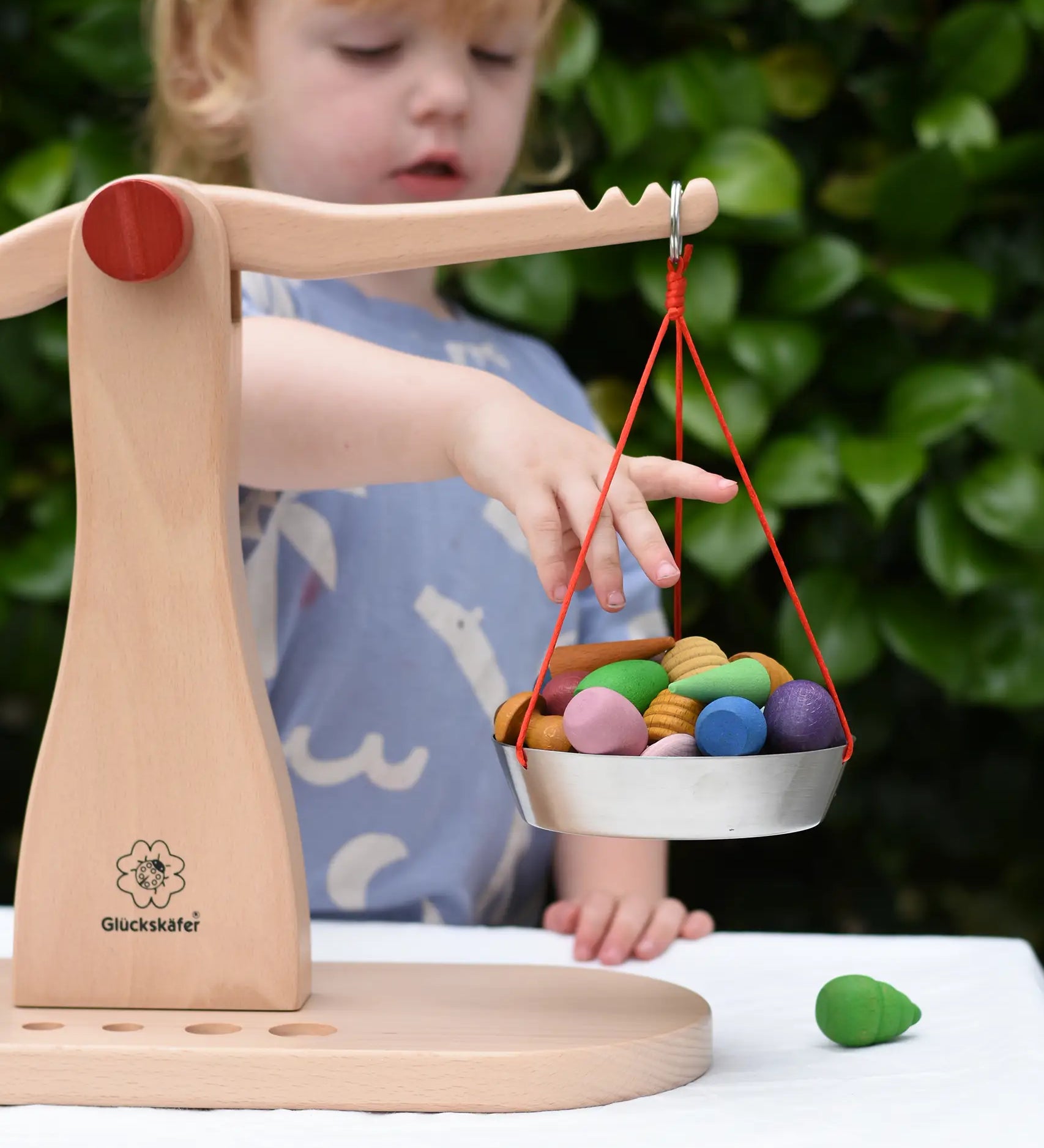 Child placing Grapat mandlaa pieces onto the Glückskäfer balance with weights children's weighing scales toy.  