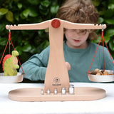 Child playing with the Glückskäfer balance with weights children's weighing scales toy.  One side has a Holztigher spinosaurus dinosaur figure and the other has Grapat mushroom mandala pieces. 