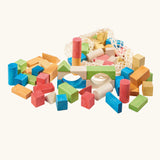 White mesh drawstring bag filled with Glückskäfer colorful wooden blocks next to a pile of wooden blocks. Glückskäfer Wooden Bio Geometric Building Blocks, 58 Piece Set.