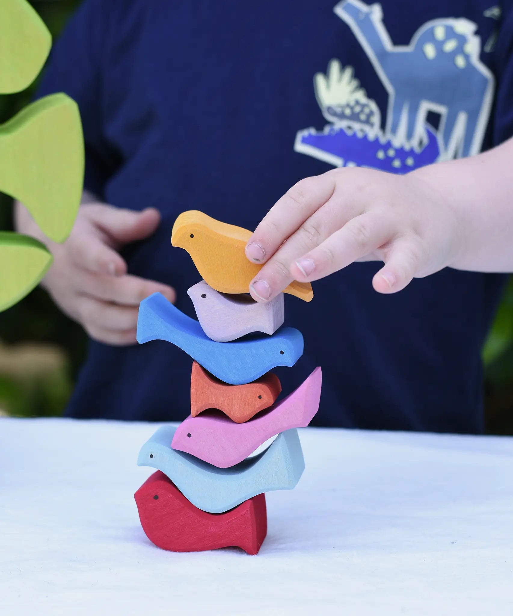 Child stacking the colourful wooden bird shaped pieces from the Glückskäfer light green wooden bird tree puzzle stacker toy on top of each other. 
