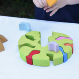 The tree part from the Glückskäfer light green wooden bird tree puzzle stacker toy placed flat on a table. A child is placing the bird shaped pieces inside. 
