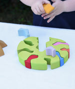 The tree part from the Glückskäfer light green wooden bird tree puzzle stacker toy placed flat on a table. A child is placing the bird shaped pieces inside. 