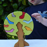 Glückskäfer light green wooden bird tree puzzle stacker toy, a child is reaching for the tree.