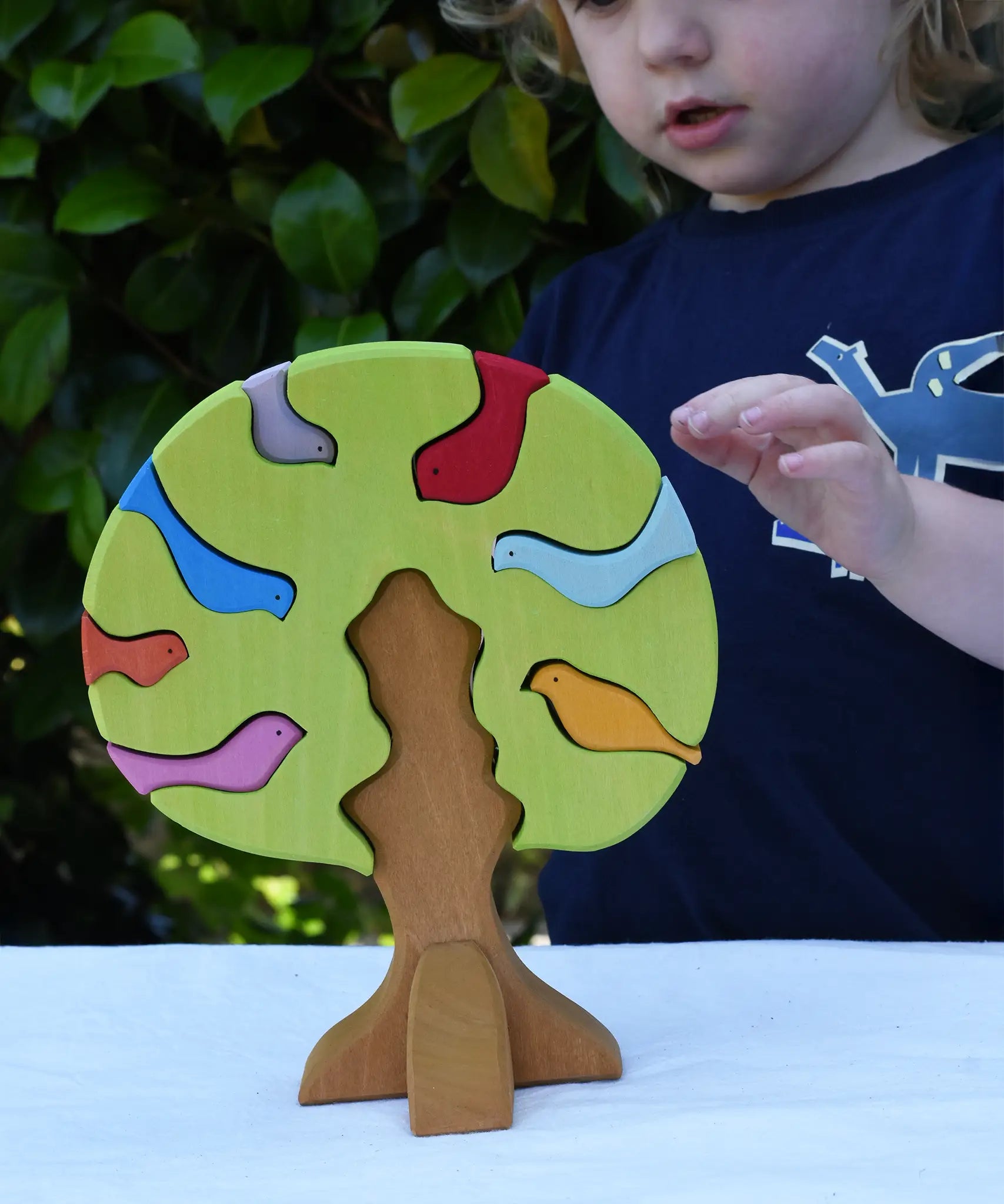 Glückskäfer light green wooden bird tree puzzle stacker toy, a child is reaching for the tree.