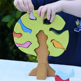 Child playing with the Glückskäfer light green wooden bird tree puzzle stacker toy, placing the bird shaped pieces into the slots.