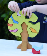 Child playing with the Glückskäfer light green wooden bird tree puzzle stacker toy, placing the bird shaped pieces into the slots.