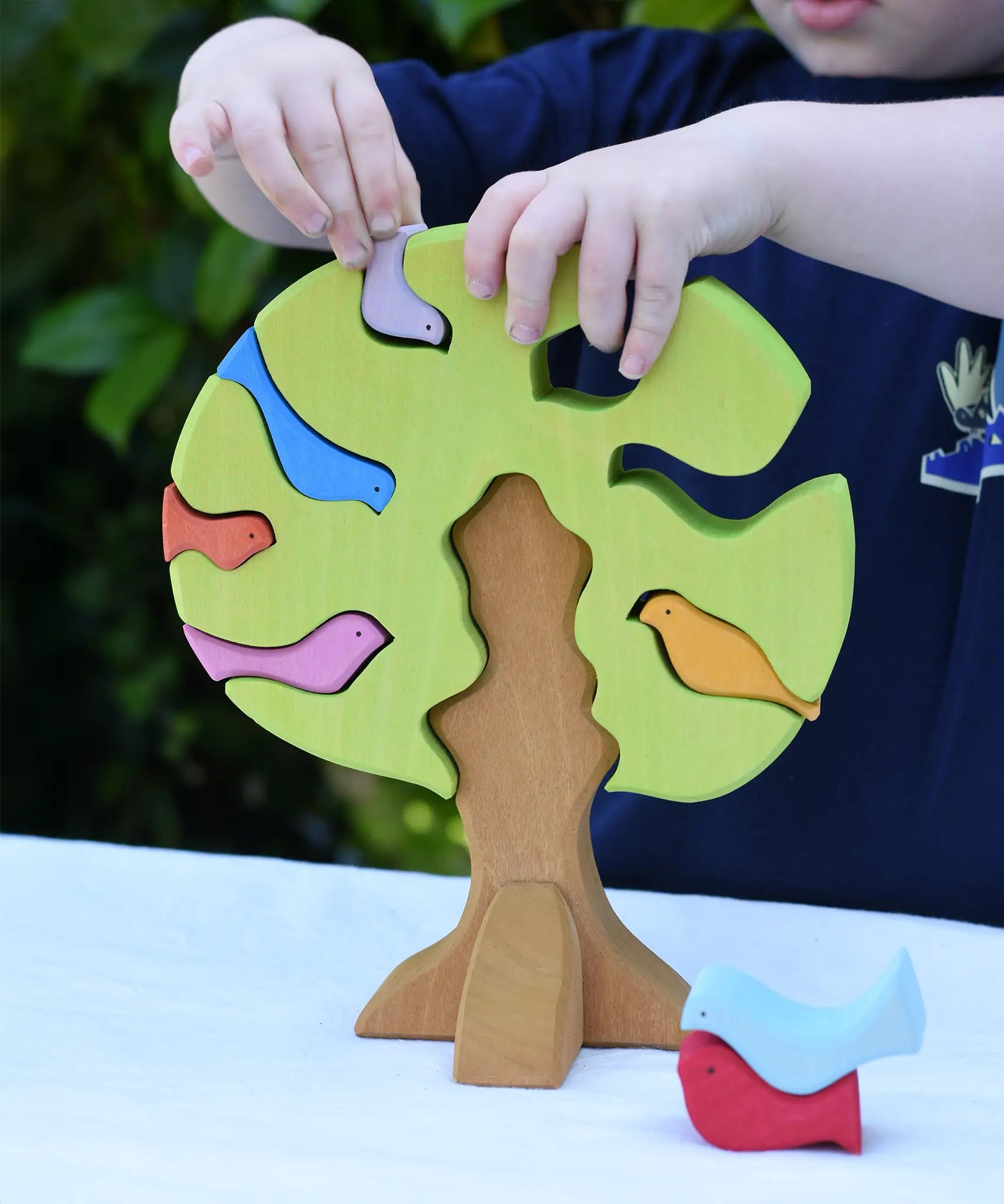 Child playing with the Glückskäfer light green wooden bird tree puzzle stacker toy, placing the bird shaped pieces into the slots.