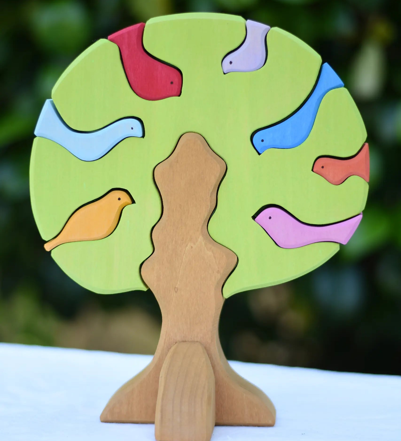 Glückskäfer light green wooden bird tree puzzle stacker toy placed on a table outdoors.
