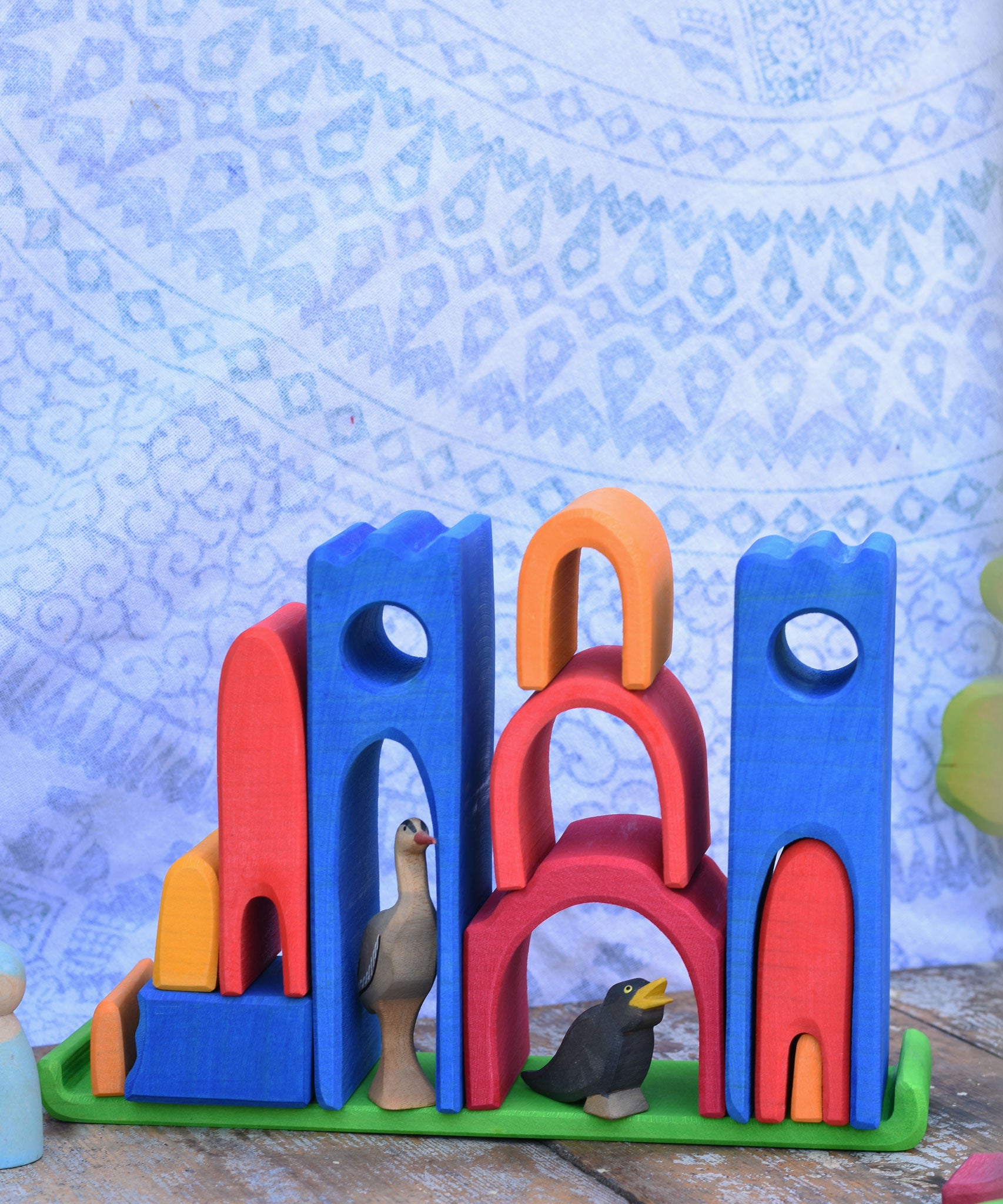 The pieces from the Gluckskafer castle stacked on the green coloured base piece. There are wooden bird figures laced underneath the arches. 