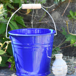 A Glückskäfer Blue Metal Bucket placed on a slate surface next to a Babipur seedbom seed packet.
