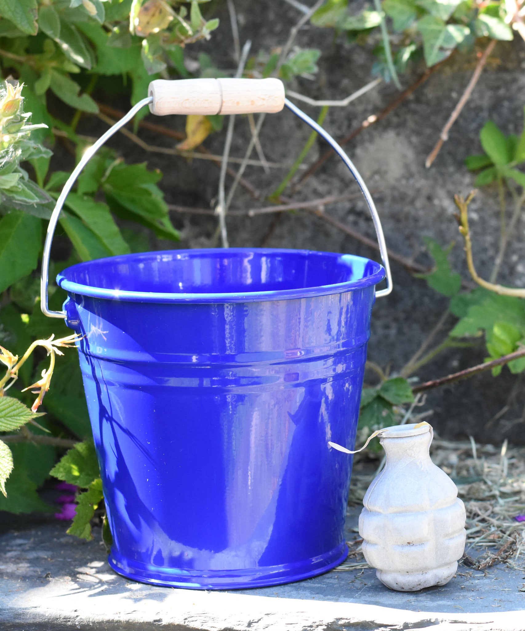 A Glückskäfer Blue Metal Bucket placed on a slate surface next to a Babipur seedbom seed packet.