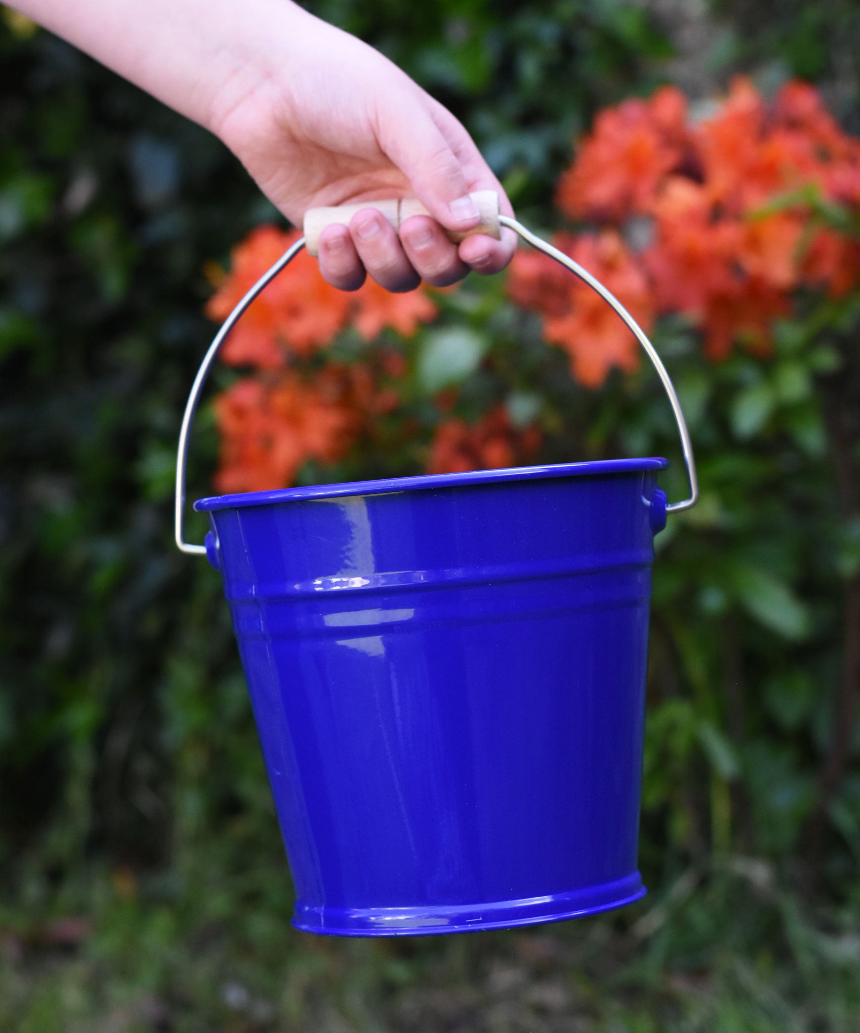A close up of a Glückskäfer Blue Metal Bucket in a child's hand. 