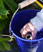 A close up of a child's hand placing a seedbom container into Glückskäfer Blue Metal Bucket.