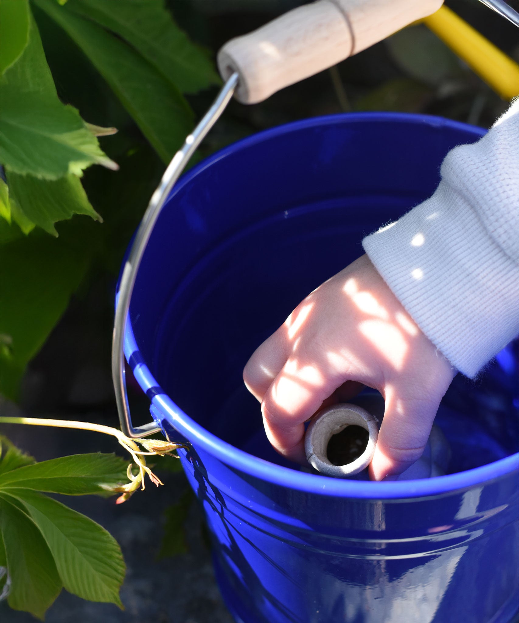 A close up of a child's hand placing a seedbom container into Glückskäfer Blue Metal Bucket.