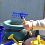 A child holding up a blue Glückskäfer Metal Blue Rake in their hand.