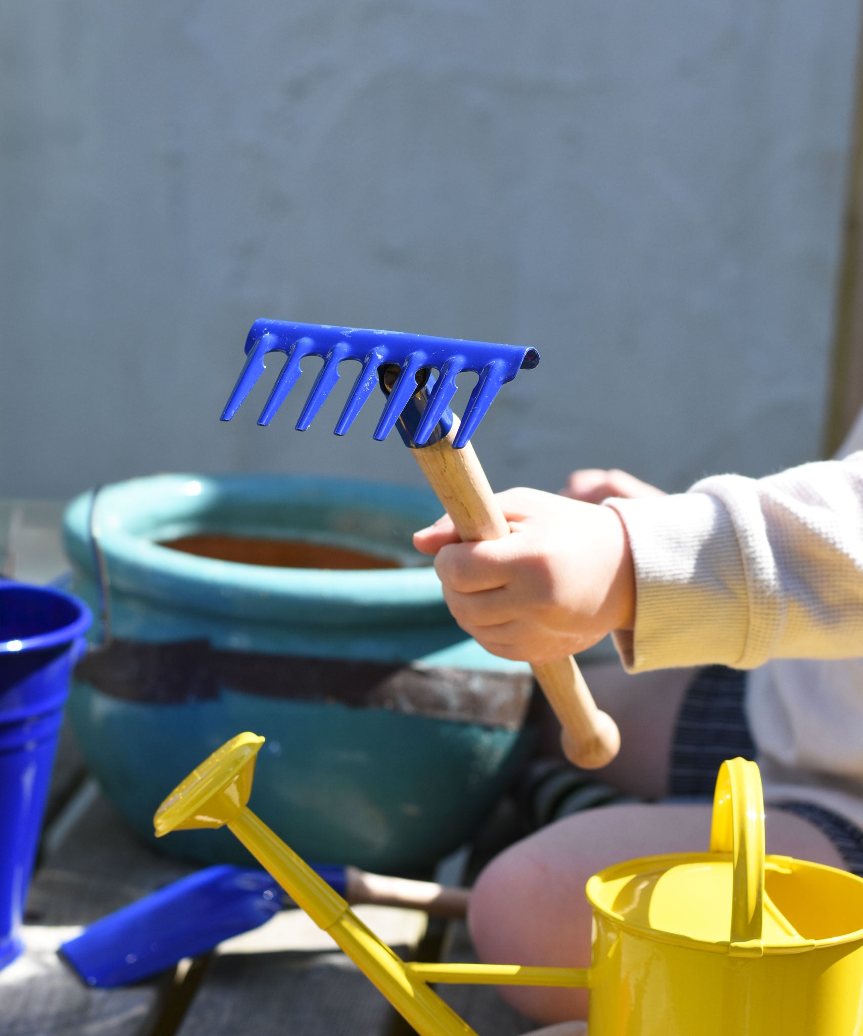 A child holding up a blue Glückskäfer Metal Blue Rake in their hand.