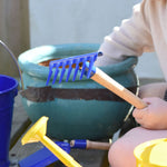A child holding up a blue Glückskäfer Metal Blue Rake in their hand.