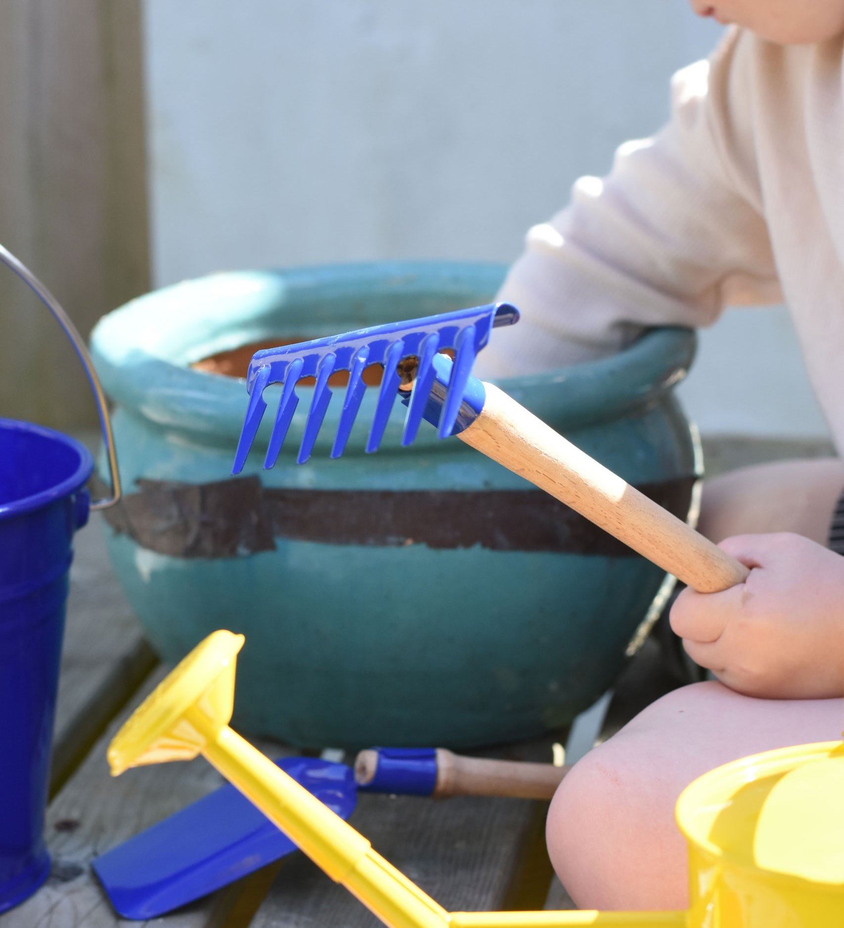 A child holding up a blue Glückskäfer Metal Blue Rake in their hand.
