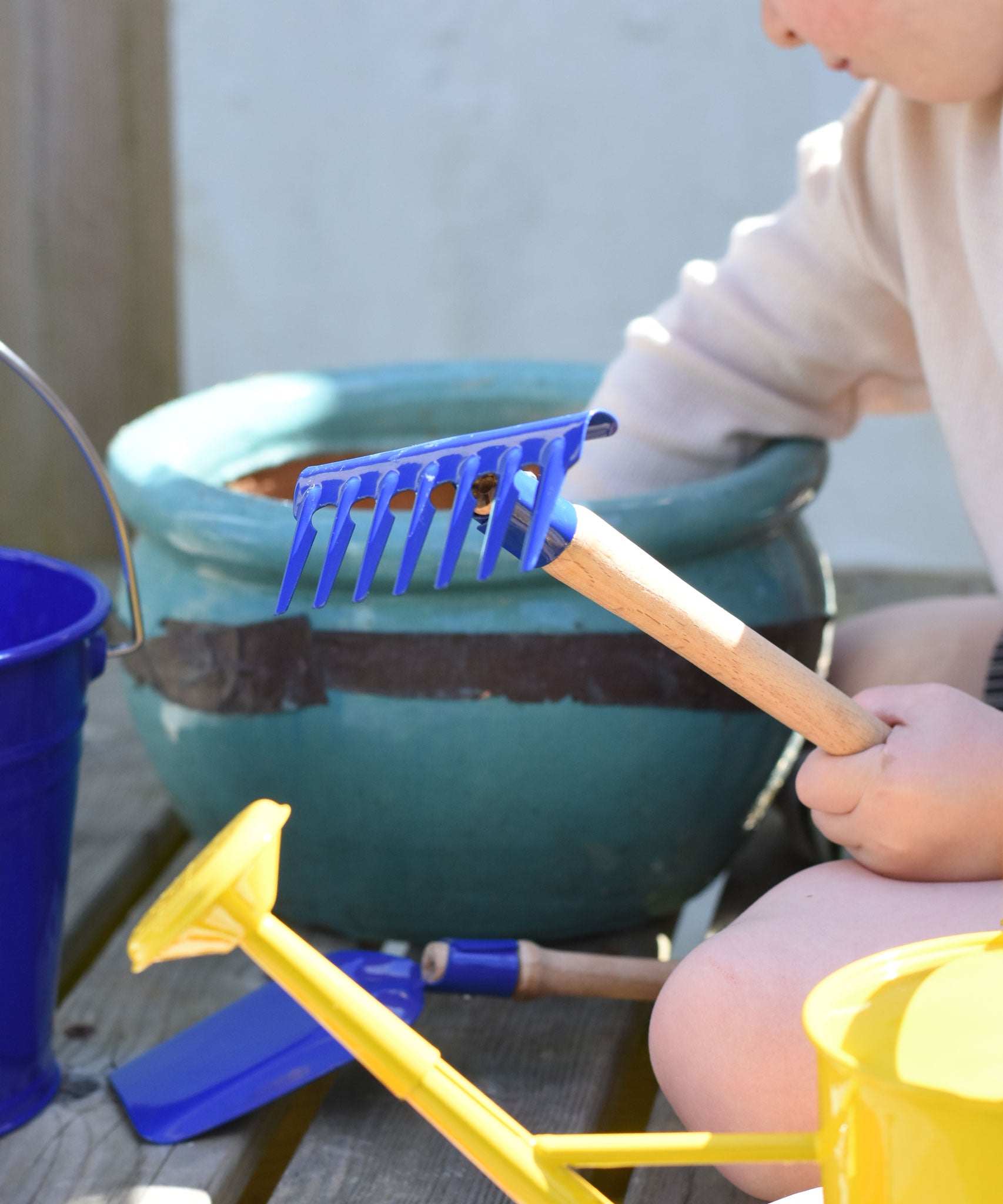 A child holding up a blue Glückskäfer Metal Blue Rake in their hand.
