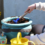 A child raking soil in a pot using a blue Glückskäfer Metal Blue Rake.