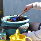 A child raking soil in a pot using a blue Glückskäfer Metal Blue Rake.