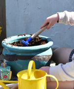 A child raking soil in a pot using a blue Glückskäfer Metal Blue Rake.