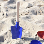 A Glückskäfer Round Metal Blue Shovel placed in the sand.