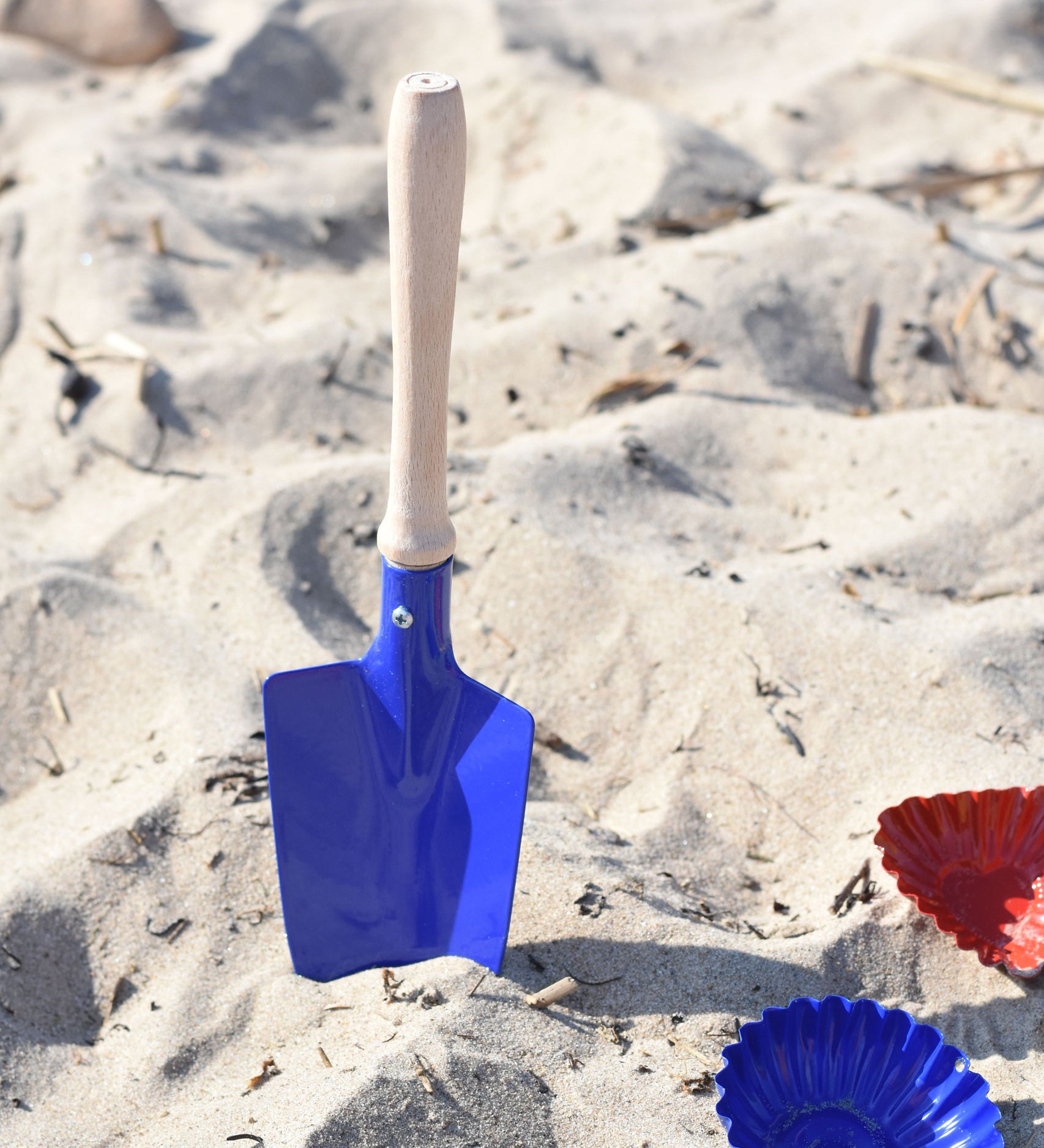 A Glückskäfer Round Metal Blue Shovel placed in the sand.
