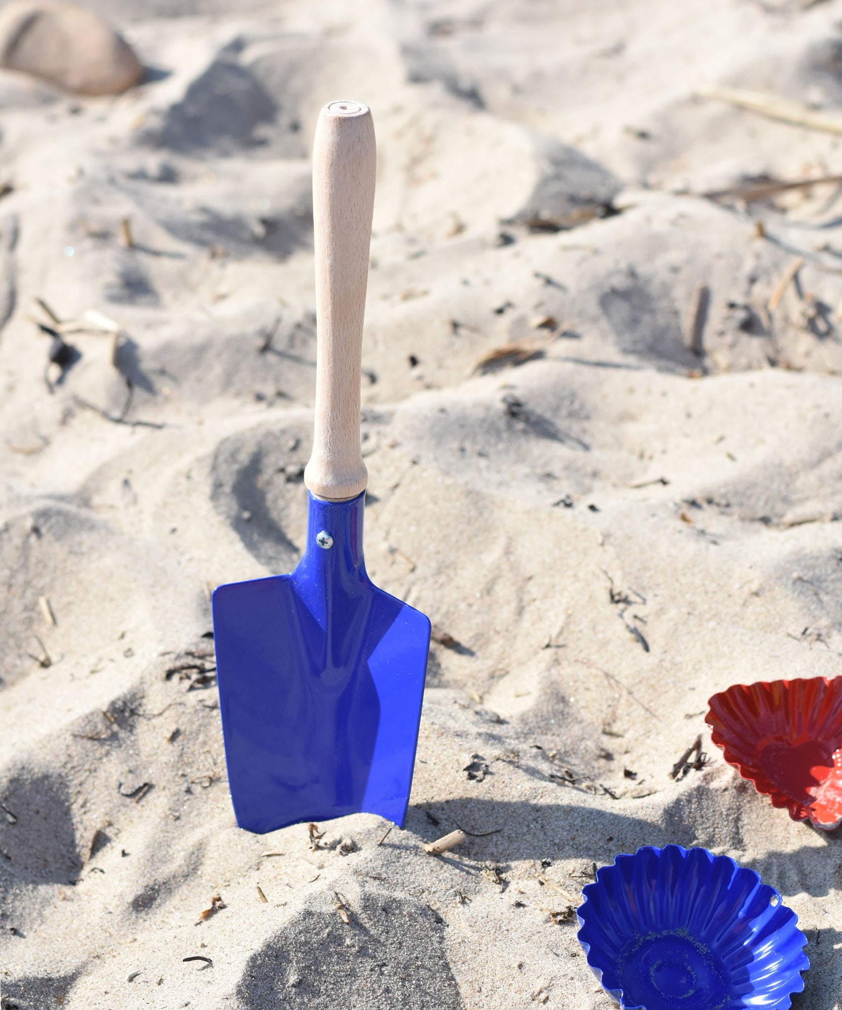 A Glückskäfer Round Metal Blue Shovel placed in the sand.