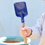 A child holding a Glückskäfer Square Metal Blue Shovel in their hand.